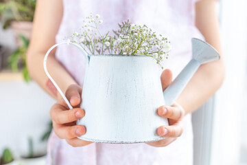 Vintage white watering can with gypsophila flowers in hands close-up. The concept of plant care, lifestyle, gardening, floristry, hobbies. Spring postcard. Plant flower shop. Mockup, copy space. © Natalia