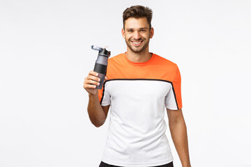 Fototapeta na wymiar Fitness trainer remind you drink water. Handsome smiling, cheerful sportsman in activewear, finish morning jogging, workout gym practice, grin joyful, holding bottle, standing white background