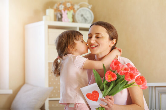 Happy Mother's Day. The child daughter congratulates her mother and gives her a homemade card and flowers pink tulips