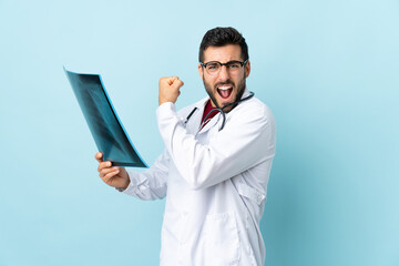 Professional traumatologist holding radiography isolated on blue background making strong gesture