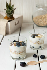 Two glasses with layered yogurt, oats and fruits, on white wooden table. Healthy breakfast, healthy lifestyle concept