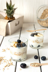 Two glasses with layered yogurt, oats and fruits, on white wooden table. Healthy breakfast, healthy lifestyle concept