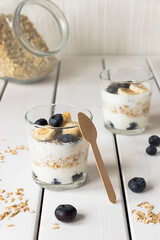 Two glasses with layered yogurt, oats and fruits, on white wooden table. Healthy breakfast, healthy lifestyle concept
