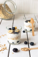 Two glasses with layered yogurt, oats and fruits, on white wooden table. Healthy breakfast, healthy lifestyle concept
