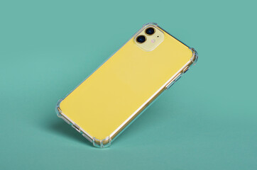 Yellow iPhone 11 in clear silicone case falls down isolated on green background back view. Phone case mockup - obrazy, fototapety, plakaty