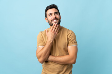 Young handsome man with beard over isolated background looking up while smiling