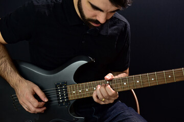 Young man playing black guitar on black background.