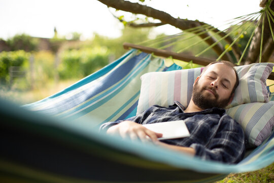 Serene man with digital tablet sleeping in backyard summer hammock