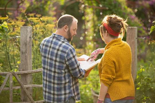 Couple with gardening book planning in sunny backyard