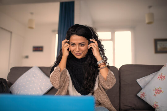 Smiling woman with headphones working from home at laptop on sofa