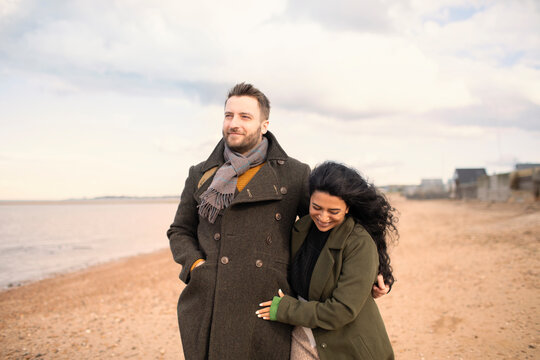 Happy couple in winter coats walking on ocean beach