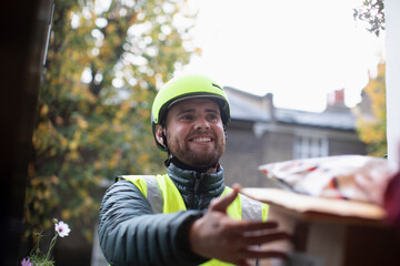 Happy friendly male courier in helmet making delivery at front door