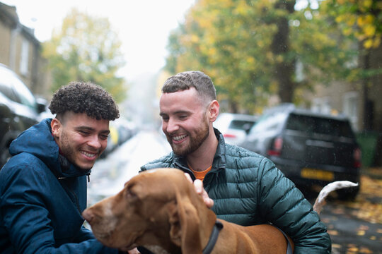 Happy gay male couple with dog on wet urban street