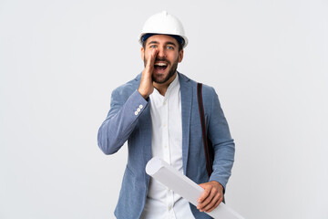 Young architect man with helmet and holding blueprints isolated on white background shouting with mouth wide open