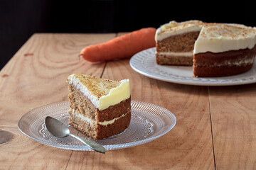 A slice of homemade carrot cake on a plate with a spoon. Background: the cake and a carrot.