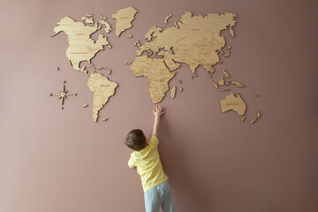 Little boy trying to get hold of a wooden world map on the wall
