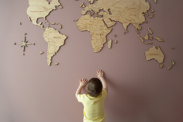 Little boy trying to get hold of a wooden world map on the wall