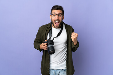 Photographer man over isolated purple background celebrating a victory in winner position