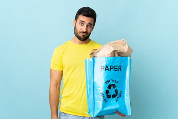 Young caucasian man holding a recycle bag isolated on blue background with sad expression