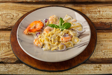 Pasta with shrimps in a creamy sauce, decorated with spinach on a gray plate on a wooden table on a stand.