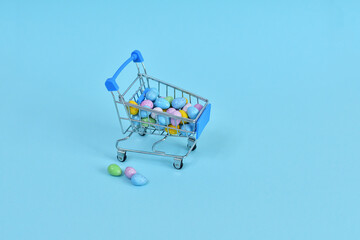 Shopping trolley with multicolored easter eggs on blue background. Easter sale.