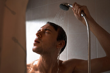 Portrait of young handsome man washes himself with shower gel, lathers head with shampoo in the...