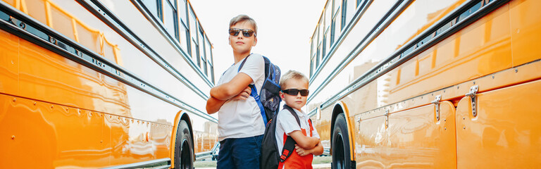  Caucasian brothers students near yellow school bus. Cool kids in sunglasses going back to school in September. Education system and learning. Support and friendship. Web banner header.