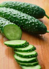 Set of fresh whole and sliced cucumbers on a wooden board with water drops. Garden cucumber wallpaper backdrop design
