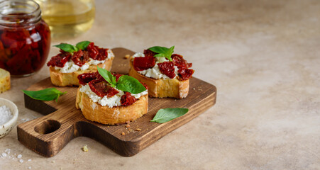 Bruschetta with sun dried tomatoes, cream cheese and basil on a wooden board. Selective focus. Copy space