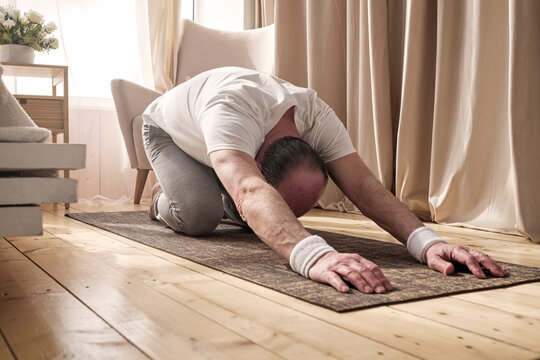 Active senior man doing the child pose while practicing yoga on a mat