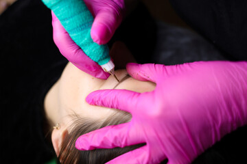 A permanent makeup artist tightens the skin near the eyebrows to perform the tattoo procedure....