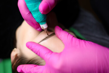 A permanent makeup artist tightens the skin near the eyebrows to perform the tattoo procedure....