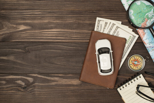 Overhead photo of brown passport wit money dollars cash inside car map magnifier compass notepad and glasses isolated on the wooden backdrop with empty space