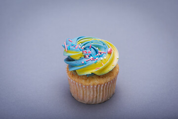 Close up of multicolored creamy cupcake with decorations with colorful stars, delicious and fabulous. Top view on gray background. Concept of birthday, celebration, sweet.