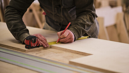 Close up. Carpenter holding a measure tape on the work bench. Woodwork and furniture making concept. Carpenter in the workshop marks out and assembles parts of the furniture cabinet
