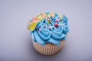 Close up of multicolored creamy cupcake with decorations with colorful stars, delicious and fabulous. Top view on gray background. Concept of birthday, celebration, sweet.