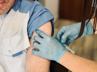 Patient receiving coronavirus vaccine in the clinic, close-up. The doctor gives an injection or vaccine into the patient's shoulder. Vaccine against Covid-19.