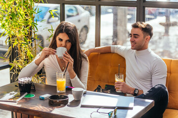 Two happy young people are laughing while sitting at a table in indoor cafe