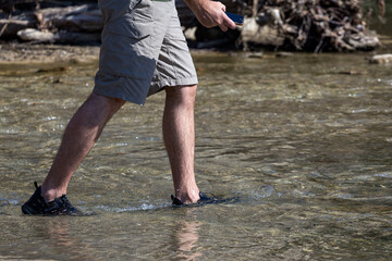 A young man taking a walk on a river, in shallow water, on a sunny day, forcing it into a ford.
