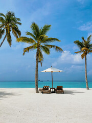 Naklejka premium Palmen, Sonnenliegen und einem Sonnenschirm auf einem Strand vor türkis blauem Wasser auf einer kleinen Insel auf den Malediven