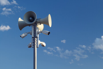 Pillar with megaphones and surveillance cameras outdoors against a blue sky during the day. Copy...
