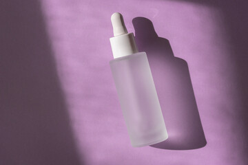 Cosmetic liquid mockup in transparent bottle on pastel lilac background, top view. Hyaluronic acid oil, serum with collagen skin care product. Mock up packaging, cosmetics branding.