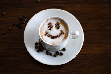 Coffee with milk and a smile in a cup. Heart made from coffee beans on a wooden table.