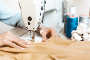 A sewing machine with the hands of a tailor, close-up. Individual designer tailoring.