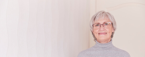 A portrait of a smiling wearing glasses elderly Caucasian woman with short gray hair on a light background. - Powered by Adobe