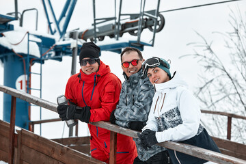 Fototapeta na wymiar group of skiers friends on the mountain are resting and drinking coffee from a thermos on the background of the ski lift
