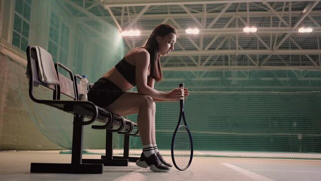 young female tennis player is sitting on bench in sporty court, training of sporty young lady