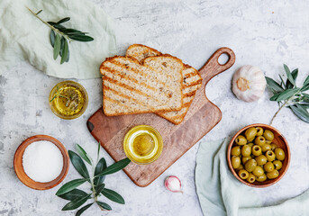 Top view olive oil, olives, toast bread and leaves on white background, space for text