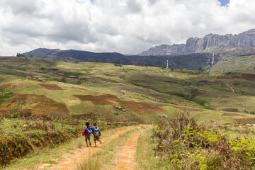 Two kids walking in a valley in front of Legendary waterfall of king and queen in Andringitra mountains, Ambalavao district, Madagascar