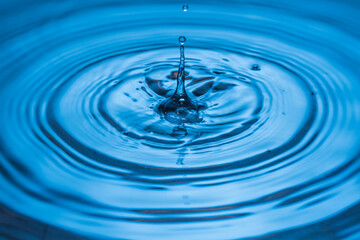 Close up view of Drops making circles on blue water surface isolated on background.